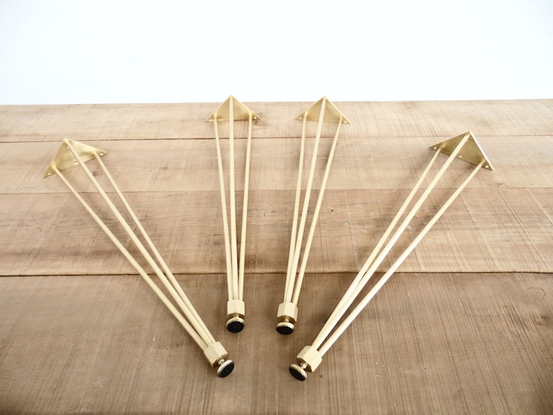 May include: Four gold metal hairpin legs for furniture. Each leg has a triangular base and three rods extending from the base.