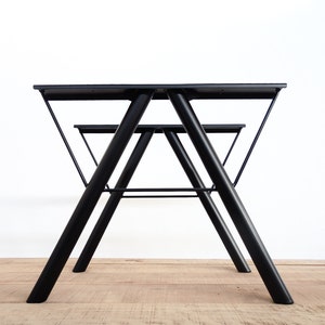 Puede incluir: Una mesa de metal negro con un marco triangular y una tapa rectangular. La mesa está hecha de metal resistente y tiene un diseño simple y moderno.