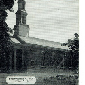 May include: Black and white photograph of the Presbyterian Church in Lyons, N. Y. The church has a tall steeple and arched windows. The image is a vintage postcard.