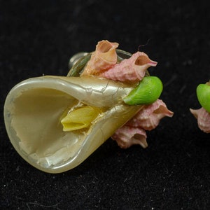 May include: A pair of vintage earrings featuring a white shell with a pink flower design. The earrings are made of metal and have a post back closure.