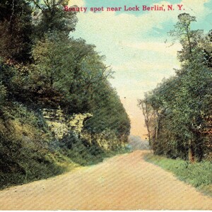 Puede incluir: Postal antigua que representa un camino de tierra que serpentea a través de un exuberante paisaje verde. La carretera está flanqueada por densos árboles y follaje, con una visión de un cielo azul. El texto en la parte superior dice "Beauty spot near Lock Berlin, N.Y."