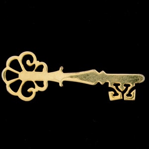 Puede incluir: Una llave de color dorado con una cabeza decorativa y adornada y un eje simple y recto.