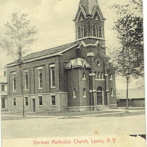 May include: A sepia-toned vintage postcard depicting the German Methodist Church in Lyons, N.Y. The church is a brick building with a prominent steeple and arched windows. The text "German Methodist Church, Lyons, N. Y." is visible at the bottom.