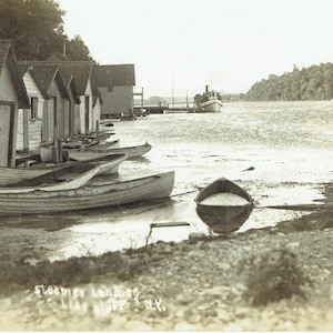 May include: A monochrome photograph depicting a waterfront scene with small wooden boats and boat houses. A steamboat is docked in the distance. The text "Steamer Landing, Hoff's N.Y." is visible at the bottom of the image.