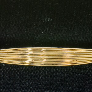 May include: A gold bangle bracelet made of multiple thin wires woven together.