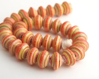 May include: A strand of colorful paper beads. The beads are cylindrical with a striped pattern in shades of orange, yellow, and green. The beads are strung together on a white string, creating a decorative accessory.