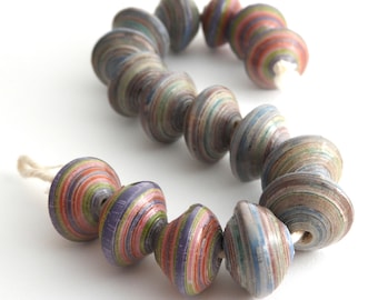 May include: A strand of colorful paper beads, each bead is made of layered paper in shades of pink, purple, green, blue, and brown. The beads are strung on a white cord.