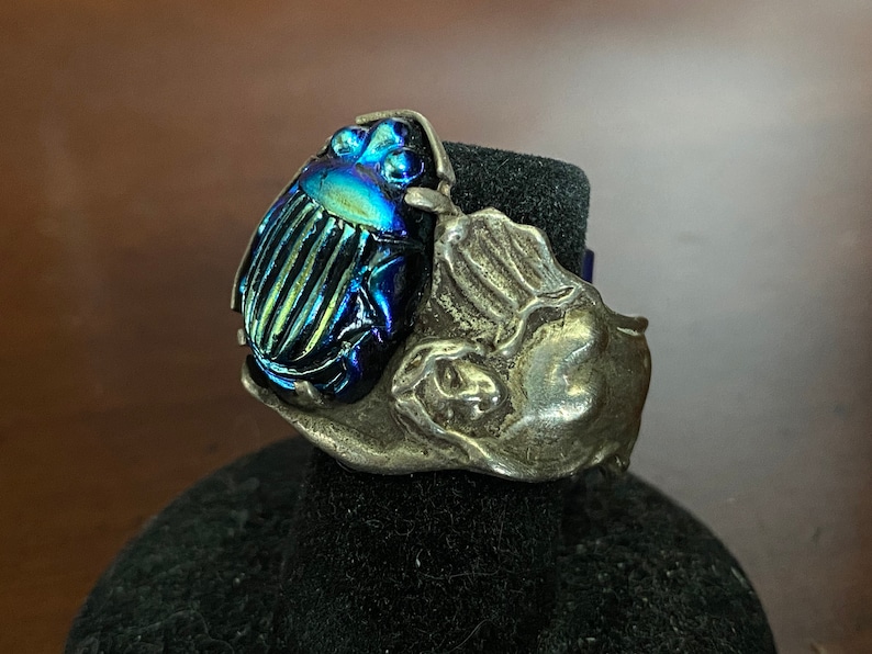 May include: A silver ring with a blue and green iridescent scarab beetle design.