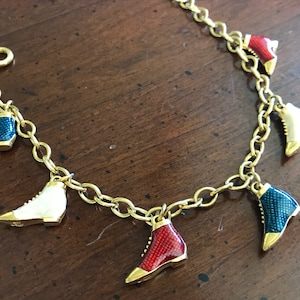 Op de afbeelding: Een gouden kettingarmband met vijf bedels in de vorm van laarzen. De laarzen zijn geëmailleerd in rood, wit en blauw.