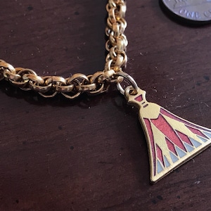 May include: A gold chain necklace with a red and white enamel pendant shaped like a pyramid. The pendant has a gold outline and a small loop at the top.