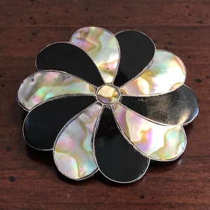 May include: A black and iridescent abalone shell flower brooch. The flower has eight petals and a center made of abalone shell.