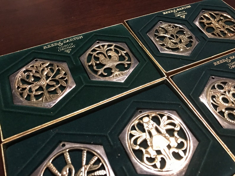 May include: Set of six silver and gold Christmas ornaments in individual boxes. Each ornament features a different design from the 12 Days of Christmas song. The boxes are lined with green velvet.