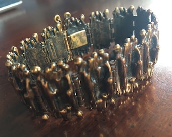 May include: A vintage bronze-toned bracelet with a textured, organic design. The bracelet features a series of interconnected rectangular links with a clasp closure. The surface has a rough, uneven texture with small, rounded protrusions.
