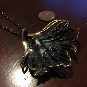 May include: A black and gold metal necklace with a large, abstract pendant. The pendant is shaped like a leaf with a delicate, intricate design.