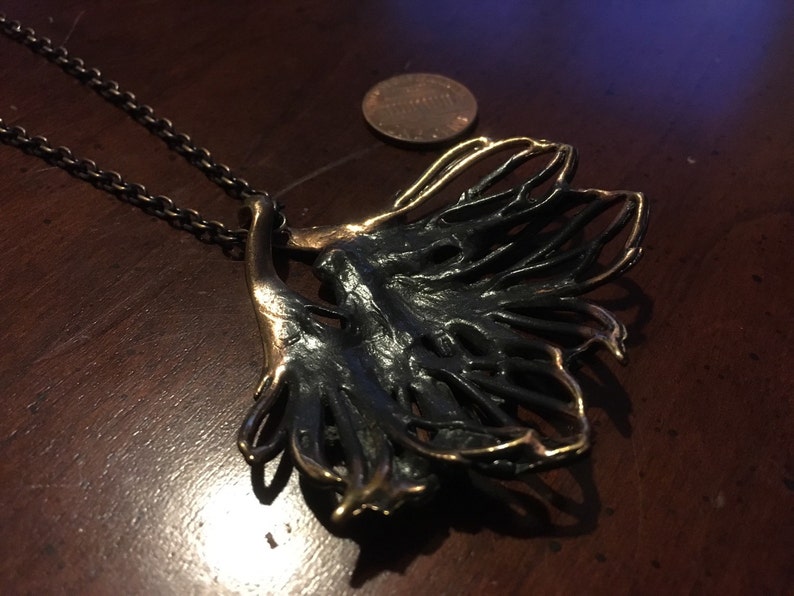 May include: A black and gold metal necklace with a large, abstract pendant. The pendant is shaped like a leaf with a delicate, intricate design.