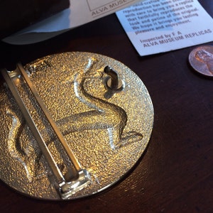 May include: A silver-toned metal belt buckle with a detailed design of a mythical creature. The buckle has a hinged pin and a loop for attaching to a belt.