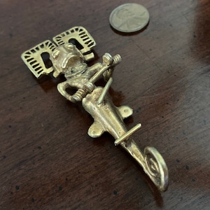 May include: A gold-colored metal figurine of a mythical creature playing a musical instrument. The figurine is detailed with intricate carvings and has a long, curved tail.