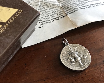 Puede incluir: Un colgante de plata con un diseño detallado de una menorá, un símbolo de la fe judía. El colgante está sobre una superficie de madera con un trozo de papel con texto sobre el Museo Judío de Nueva York.