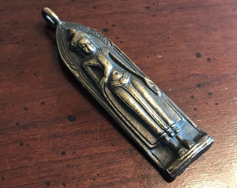 May include: A gold-toned metal pendant featuring a detailed relief of a standing Buddha figure. The pendant is shaped like a rectangular arch and has a loop at the top for hanging.