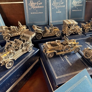 May include: A collection of silver car miniatures in display boxes. The boxes are blue with silver lettering that reads "Silver Car Miniatures". The miniatures are detailed and realistic, with intricate designs and features.
