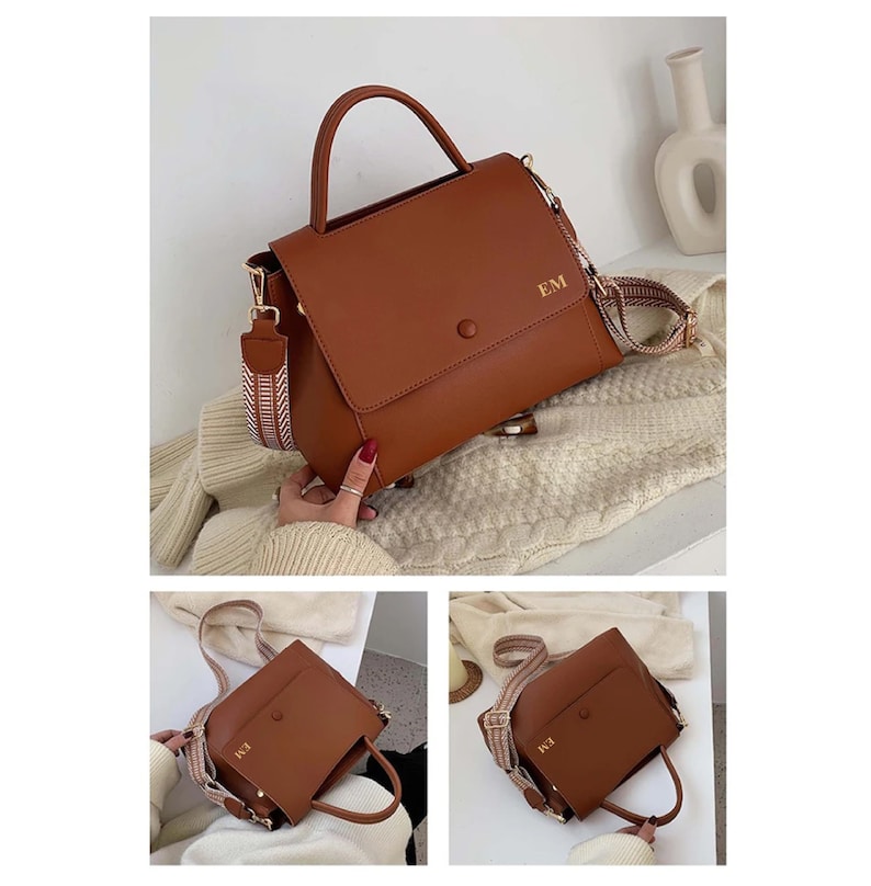 May include: A brown handbag with a top handle and a detachable shoulder strap. The bag features a flap closure and the initials "EM" in gold. The strap has a woven pattern in shades of brown and cream.