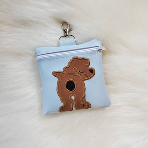 May include: A light blue zippered pouch with a brown embroidered dog design. The pouch has a silver clip for attaching to a leash or belt loop.