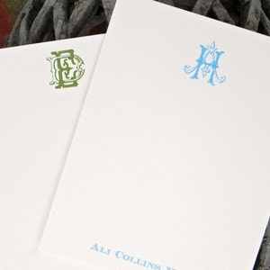 May include: Two white stationery cards with blue and green monograms. The top card has a blue monogram with the letter "A" and the text "Ali Collins Hunt". The bottom card has a green monogram with the letter "E" and the text "Elizabeth Dura."