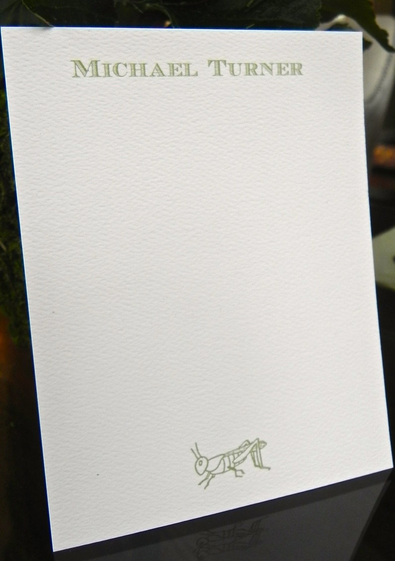 May include: A white card with the name "MICHAEL TURNER" printed in green at the top. A green line drawing of a grasshopper is at the bottom of the card.