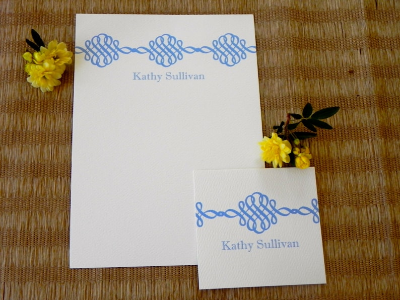 Peut inclure: Deux cartes de correspondance blanches avec des bordures d&eacute;coratives bleues et le nom "Kathy Sullivan" imprim&eacute; sur chacune. La plus grande carte est une feuille de papier pleine, tandis que la plus petite carte est une carte pli&eacute;e.