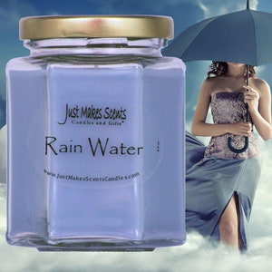 May include: A glass jar candle with a blue wax and a gold lid. The label reads "Just Makes Scents Candles and Gifts" and "Rain Water" with the website address "www.JustMakesScentsCandles.com".