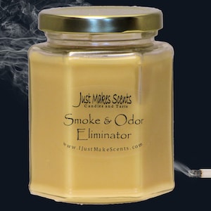 May include: A glass jar candle with a gold lid. The candle is yellow and has the text "Just Makes Scents Candles and Tarts Smoke & Odor Eliminator www.JustMakesScents.com" on the label. A lit cigarette with smoke is in the background.