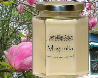 May include: A hexagonal glass jar candle with a gold lid. The candle is labeled "Just Makes Scents Candles and Tarts" and "Magnolia". The website address "www.iJustMakeScents.com" is printed on the label.