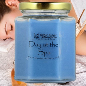 以下が含まれることがあります： 金色の蓋が付いた青いガラスのジャーキャンドル。キャンドルには「Just Makes Scents Candles and Tarts」と「Day at the Spa」のラベルが貼られており、ウェブサイト「www.justmakescents.com」が記載されています。