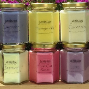 May include: Six hexagonal glass jars with gold lids filled with scented candles. The candles are labeled with the scents: Lavender, Honeysuckle, Gardenia, Jasmine, Fresh Cut Roses, and Lilac.