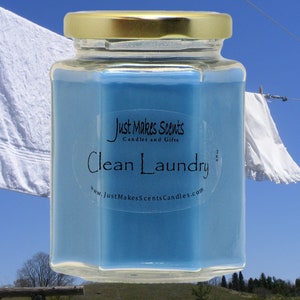 以下が含まれることがあります： 青いワックスと金の蓋が付いたガラス製のキャンドルが入った瓶。ラベルには「Just Makes Scents Candles and Gifts」と「Clean Laundry」とウェブサイトのアドレス「www.JustMakesScentsCandles.com」が書かれています。