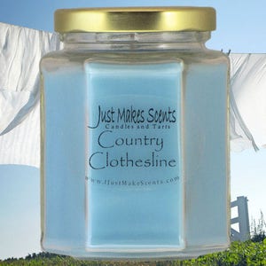 May include: A blue glass candle jar with a gold lid. The label reads "Just Makes Scents Candles and Tarts Country Clothesline www.JustMakesScents.com".
