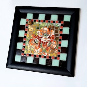 May include: Square mosaic art piece with a black frame. The mosaic features a floral design with orange and red flowers. The border has a checkerboard pattern of black, brown, and light green tiles. A small, round, gold-colored embellishment is in the upper left corner.
