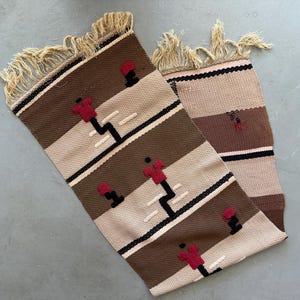 May include: A woven rug with a geometric pattern in brown, beige, and red. The rug has a fringe on both ends.
