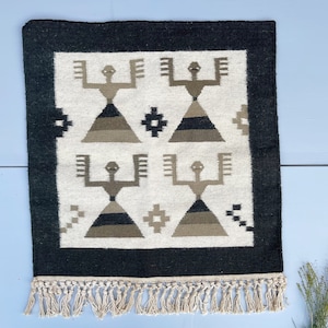 May include: A black and white rug with a geometric pattern of stylized figures. The rug has a fringe border.
