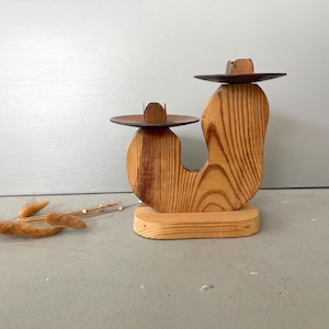 May include: A wooden candle holder with two metal candle cups. The holder is shaped like a stylized 'U' and has a natural wood finish.