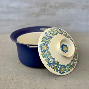 May include: A blue and white ceramic serving bowl with a lid. The lid has a floral design with blue, green, and white flowers. The bowl has a blue rim and a white interior.