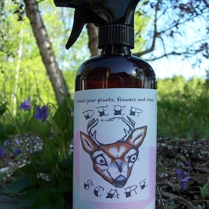Puede incluir: Una botella de spray de vidrio marr&oacute;n con un pulverizador de gatillo negro. La etiqueta es rosa y blanca con un ciervo de dibujos animados y el texto "Proteja sus plantas, flores y &aacute;rboles Espantap&aacute;jaros de ciervos Previene da&ntilde;os por ciervos, conejos y ardillas".