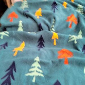 May include: A teal blue fleece blanket with a repeating pattern of colorful trees. The trees are in shades of orange, yellow, and green.