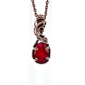 May include: A copper pendant necklace with a striking red gemstone. The oval-shaped gemstone is intricately wire-wrapped in copper. The pendant is suspended from a fine copper chain, offering a sophisticated and attractive jewellery item.
