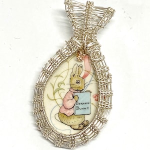 May include: A silver wire wrapped pendant featuring a vintage illustration of a rabbit holding a book that says "Benjamin Bunny".