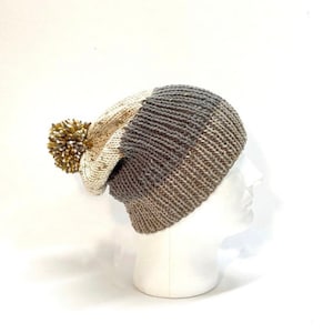 May include: A gray and white knit beanie with a fluffy pom pom on top. The beanie is made of a soft, warm yarn and has a slouchy fit.