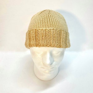 Puede incluir: Un gorro de punto beige con borde de canalé.