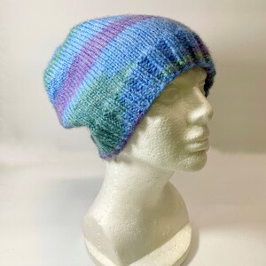 May include: A blue, green, and purple striped knitted beanie hat. The hat is on a white mannequin head.