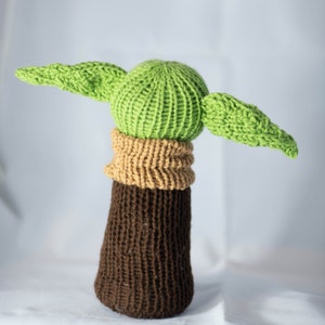 K&ouml;nnte beinhalten: Ein gestricktes gr&uuml;nes und braunes Pl&uuml;schtier mit gro&szlig;en Ohren. Das Spielzeug ist in Form eines Charakters aus dem Star Wars-Franchise.