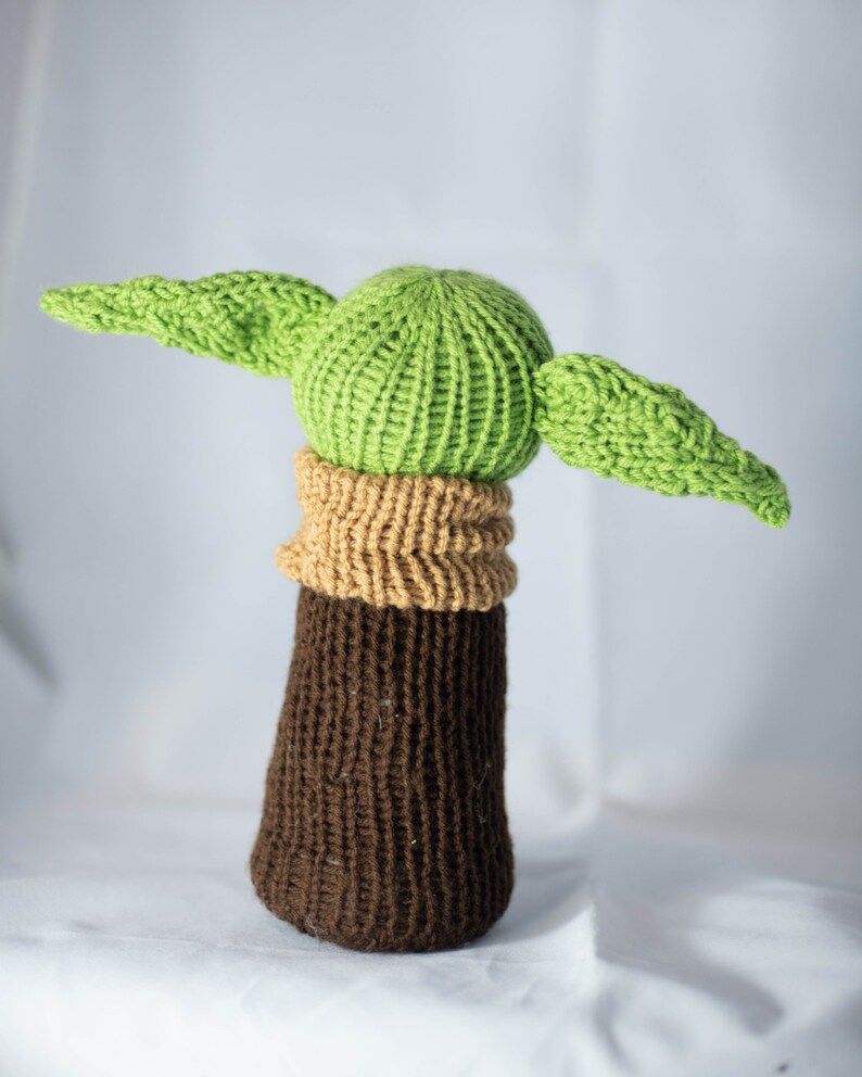 K&ouml;nnte beinhalten: Ein gestricktes gr&uuml;nes und braunes Pl&uuml;schtier mit gro&szlig;en Ohren. Das Spielzeug ist in Form eines Charakters aus dem Star Wars-Franchise.